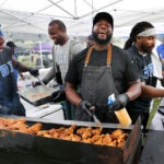 Chef Brian Alleyne, center, has a chuckle as he cooks chicken legs on his charcoal grill
